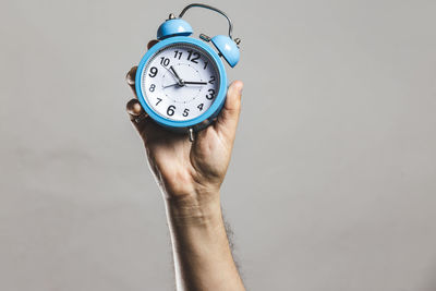 Close-up of hand holding clock against gray background