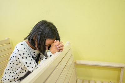 Girl praying while sitting on pew at church