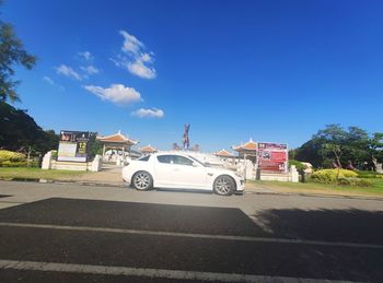 Cars on road by buildings against blue sky
