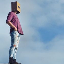 Low angle view of man wearing cardboard box on head against sky