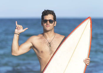 Young man holding sunglasses against sea