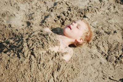 High angle view of boy covered with sand at beach on sunny day