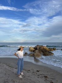 Rear view of woman standing at beach against sky