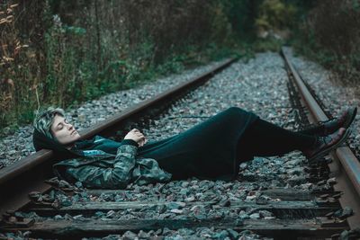 Young woman sitting on railroad track in forest