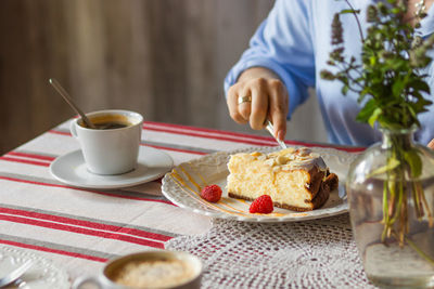 Businesswoman in blue blouse drinking morning coffee with piece of raspberry cheesecake in cafe.