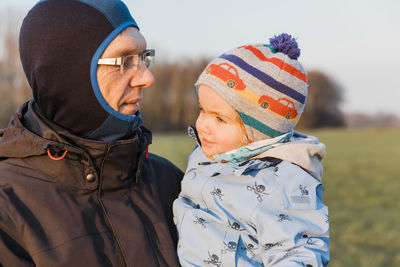 Senior man holding granddaughter while standing against agricultural field