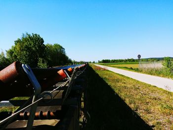 Road amidst field against clear blue sky