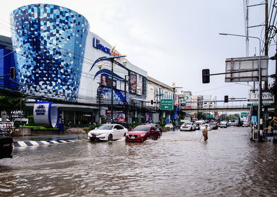 Wet street by buildings in city against sky