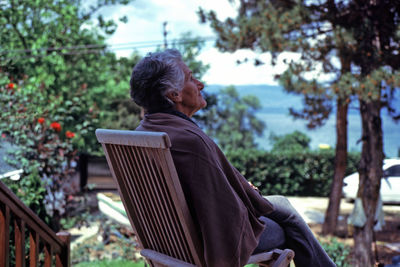 Woman sitting on bench against trees