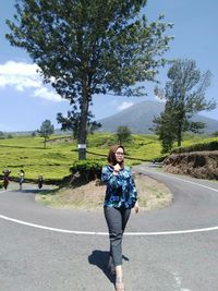 Full length portrait of young woman on road against trees