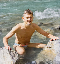 Shirtless mature man crouching in river at whiteswan lake provincial park