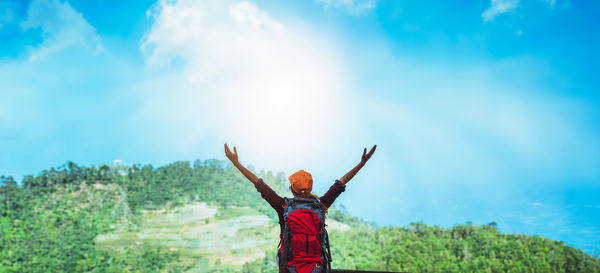 Rear view of woman with arms raised standing against sky