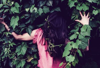 Rear view of woman gesturing against plants