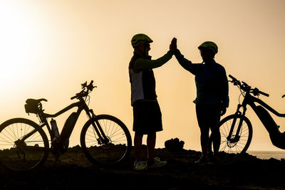 Men riding bicycle against sky during sunset