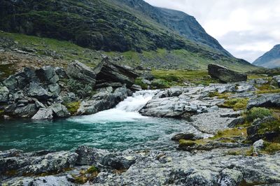 Scenic view of river, small waterfall and mountains against sky