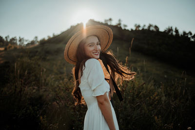 Side view portrait of smiling young woman standing on field