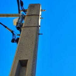 Low angle view of telephone pole against clear blue sky