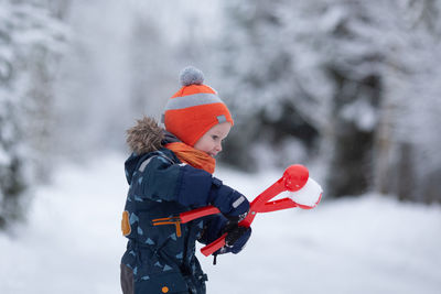 Toddler girl wearing winter clothes having fun outside in snowy day. girl is making snowballs.