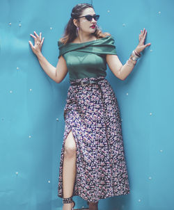 Young woman wearing sunglasses standing against blue wall