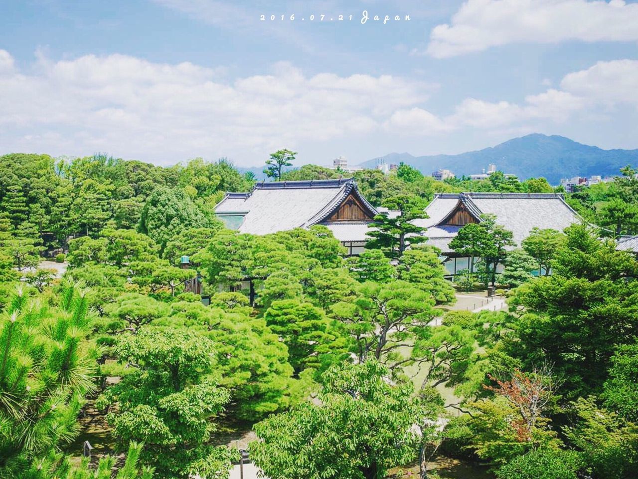 tree, architecture, built structure, sky, mountain, cloud - sky, green color, growth, cloud, lush foliage, nature, beauty in nature, plant, cloudy, day, outdoors, town, scenics, no people, tranquility, mountain range, landscape, tranquil scene, hill, green, idyllic