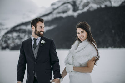 Groom in suit glances at newlywed wife in white wedding dress winter