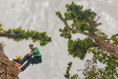 Low angle view of man standing on tree against cloudy sky