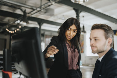 Female entrepreneur explaining male coworker over desktop pc at office