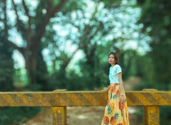 Woman standing by railing against trees