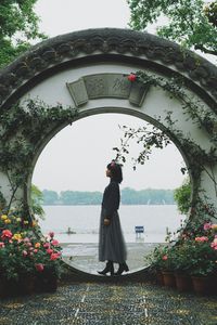 Rear view of woman standing by flowering plants against sky