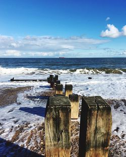 Close-up of wooden post at shore by seascape against cloudy sky