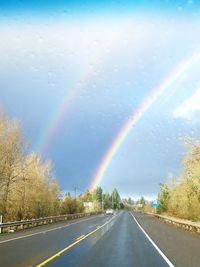 Rainbow over road against sky during rainy season