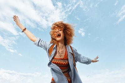 Young woman with arms raised standing against sky