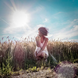 Thoughtful woman crouching on field against sky