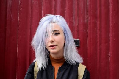 Close-up portrait of young woman against red wall