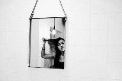 Young woman with arms raised on wall at home