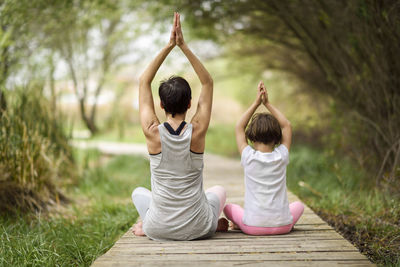 Rear view of mother and daughter doing yoga on boardwalk