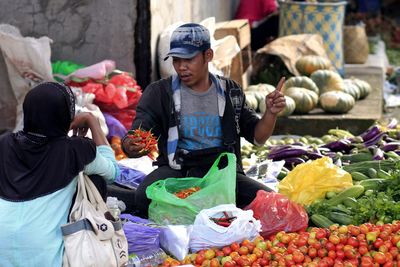 Vendor sitting at market stall with vegetables for sale