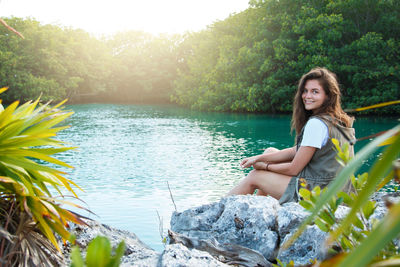 Portrait of woman sitting by lake against trees