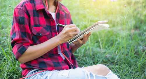Midsection of woman writing in book while sitting on grass