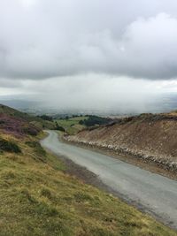 Dirt road passing through landscape against cloudy sky