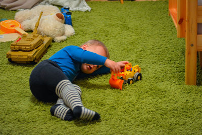 Baby boy playing with toy while lying on rug at home