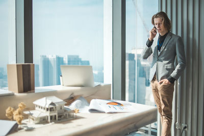 Businessman talking over mobile phone while standing by window