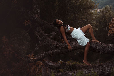 Side view of young woman lying down on tree trunk in forest