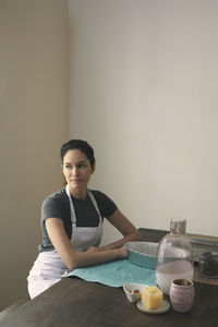 Thoughtful woman in apron sitting with containers and ingredients for preparing food at home