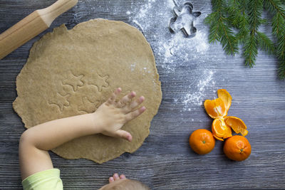 A small child and cooking gingerbread cookies in a kitchen with tangerines and a christmas tree.