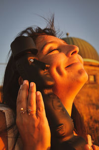 Close-up portrait of woman with hands against sky