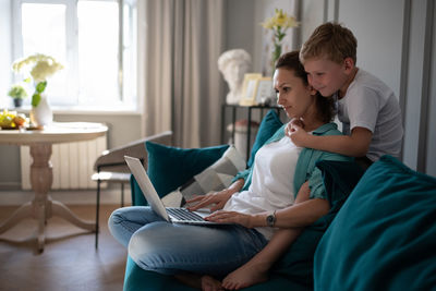 Boy hugging working mother on sofa