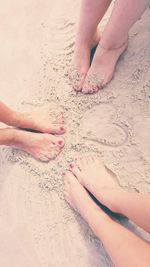 Low section of friends amidst heart shape on sandy beach