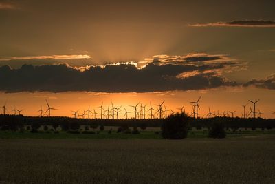 Windmills on land against sky during sunset