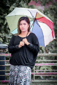 Portrait of young woman with umbrella standing outdoors